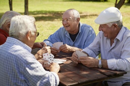 A group of senior men sits at a picnic bench playing cards